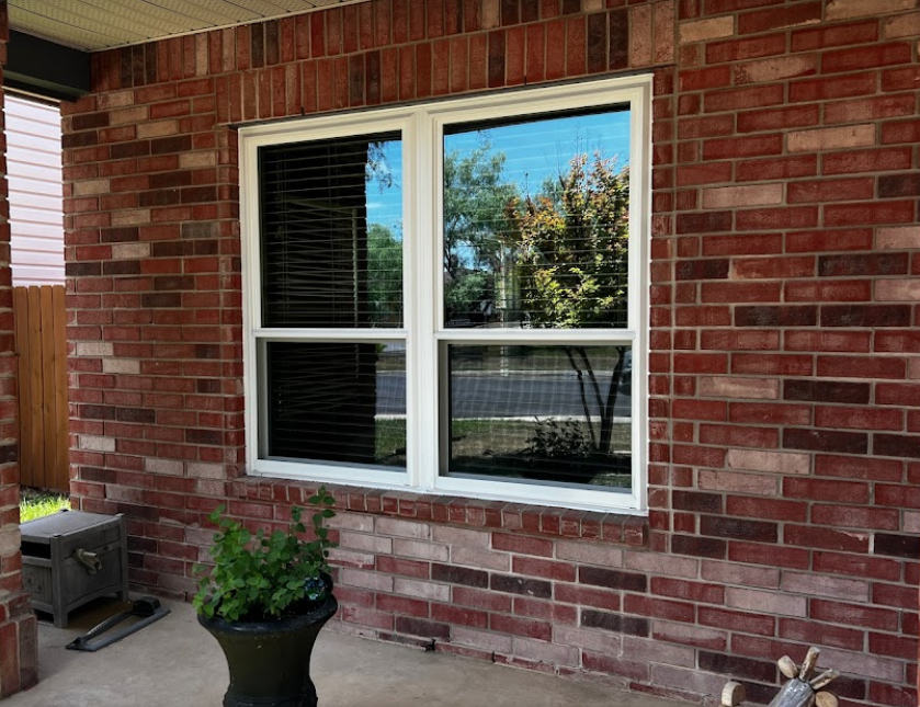 closeup of a red brick home with two windows installed that are reflecting the scenery on the outside