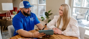 A Window World representative discusses options with a smiling homeowner at her kitchen table