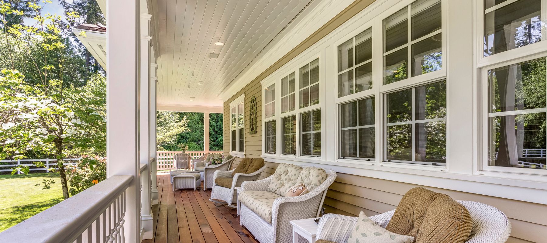 Covered front porch with white trim, wicker seating, and lush green backyard surroundings