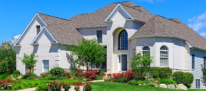 Large brick home with arched windows and a colorful landscaped front yard under a clear blue sky